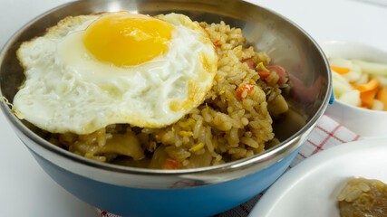 Nasi goreng or Indonesian Fried rice served with fresh tomatoes and meatballs on a white ceramic plate and pickles on a white bowl on a white background