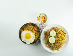 Nasi goreng or Indonesian Fried rice served with fresh tomatoes and meatballs on a white ceramic plate and pickles on a white bowl on a white background