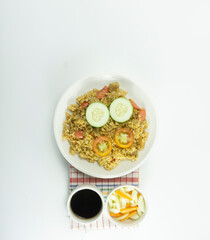 Obraz na płótnie Canvas Nasi goreng or Indonesian Fried rice served with fresh tomatoes and meatballs on a white ceramic plate and pickles on a white bowl on a white background