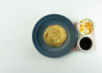 Nasi Goreng or Indonesian Fried rice served with fresh tomatoes and meatballs in a green tosca ceramic plate and pickles on a white bowl on a white background