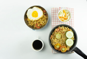 Nasi Goreng or Indonesian Fried rice served with fresh tomatoes and meatballs in a teflon bowl black tosca and pickles on a white bowl on a white background