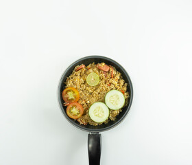 Nasi Goreng or Indonesian Fried rice served with fresh tomatoes and meatballs in a teflon bowl black tosca and pickles on a white bowl on a white background