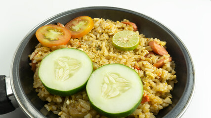 Nasi Goreng or Indonesian Fried rice served with fresh tomatoes and meatballs in a teflon bowl black tosca and pickles on a white bowl on a white background