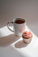 A cupcake or muffin stands next to a cup of coffee.