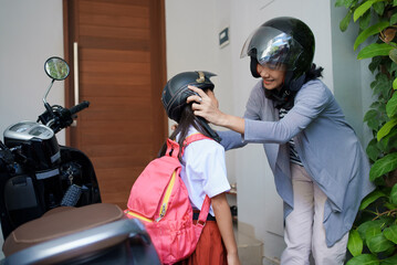 mother taking her daughter to school by motorcycle in the morning. asian primary student wearing...