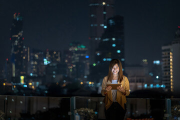 Asian businesswoman using tablet with smile action in the financial district area at bangkok river side, Thailand, technology with career concept