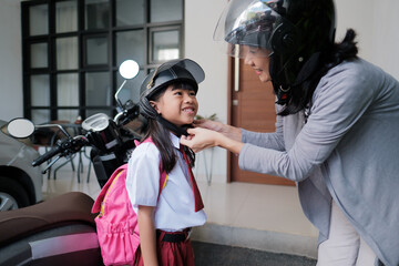 Fototapeta na wymiar asian mother fasten her daughter helmet. taking to school by motorcycle scooter in the morning. primary student going back to school