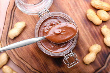 Jar and spoon with tasty chocolate paste on wooden background