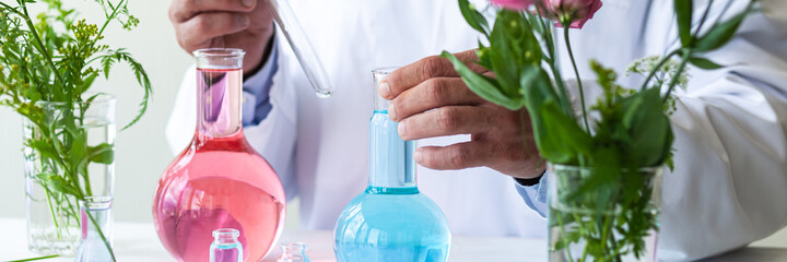 Fototapeta na wymiar Concept of herbal natural organic ingredients in cosmetic. Young man scientist in white medical gown doing laboratory research and tests with plant and flower ingredients. Close up banner