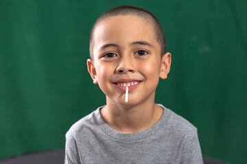 Cute caucasian young kid holding yellow lollipop showing broken milk tooth..Studio portrait, concept health with dark green background..boy in smiling face,cheeky face and funny posting.