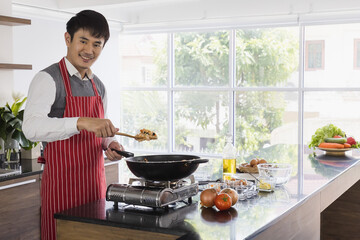 Portrait shot of Asian young handsome husband wears red stripe apron stand smiling look at camera...