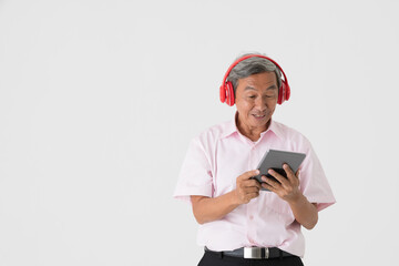 Portrait of a good-looking full of energy and active senior older Asian man holding and wearing red headphone and listening to music via tablet computer with joyfully and happy on white background.