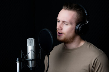Young and handsome male singer working in voice recording studio, he sings to microphone with deep...
