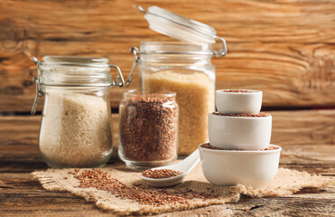 Composition with bowls and jars of flax seeds on wooden background