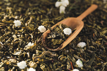Scoop on dry green tea leaves with flowers, closeup
