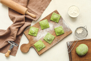 Wooden board with raw ravioli on table