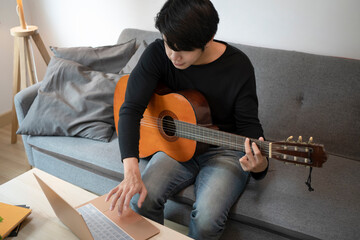 Young man using laptop computer and playing guitar on sofa.