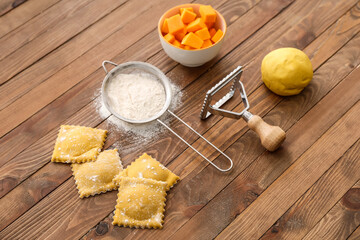 Raw ravioli, sieve and cutter on wooden table