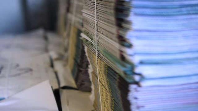 Slow pan down close up of stacks of daily newspapers bound and ready for distribution.