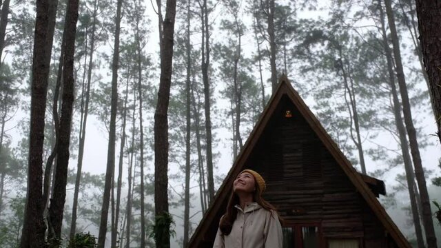 Slow motion of a young woman standing in front of a log cabin in the woods