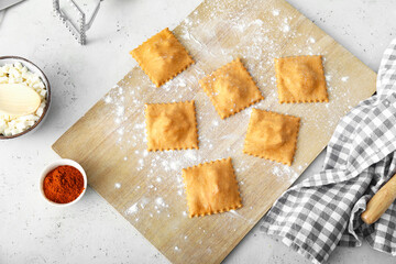 Wooden board with raw ravioli on table