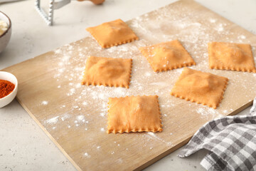 Wooden board with raw ravioli on table