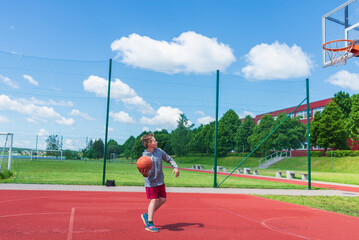 Fototapeta premium Young boy having fun playing basketball outdoors.nice,cool caucasian alone player playing basketball outdoors.