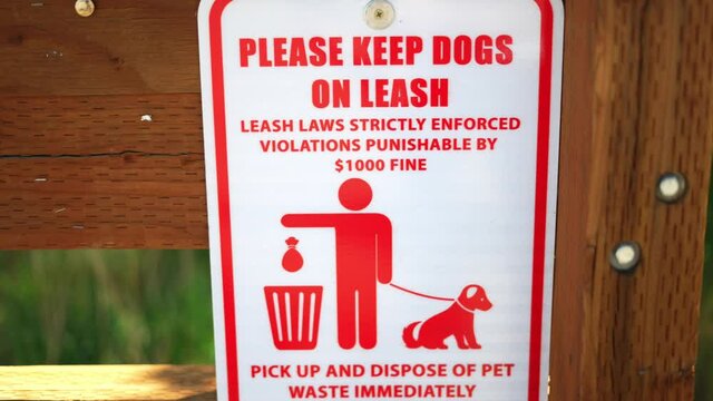 Please keep dog on leash, laws strictly enforced, violations punishable by $1000 fine, and pick up your pet waste poop sign, posted at public national park hiking trail. In 4k slow motion.