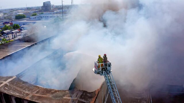 Aerial view of firemen quelling and controlling a large building on fire, from a ladder truck