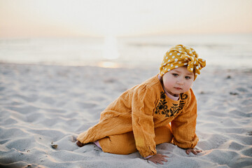 Little girl crawling on the sand on the beach during sunset