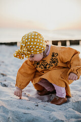 little girl running her finger along the sand on the beach during sunset