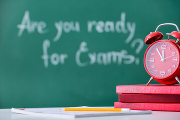 Stack of books and answer sheet forms with alarm clock on table in classroom