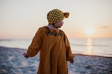 Little girl walking along the beach and turning to the water and the sun