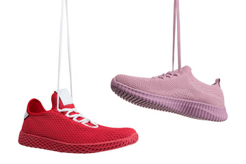 two summer sneakers made of mesh material, one red the other pink, hang on laces, on a white...