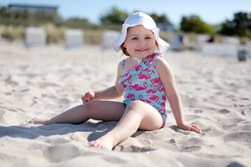Little happy smiling girl sitting on white sand beach