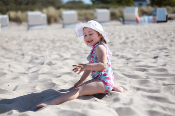 Little laughing girl on white sand beach enjoying summer and vacation