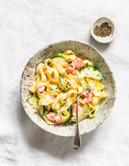 Fresh tagliatelle pasta with salmon and zucchini in cream sauce on a light background, top view
