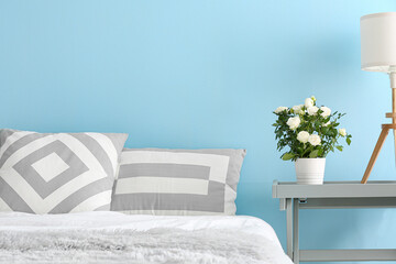 Bed and white roses in pot on table near color wall