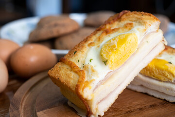 Croque madame or monsieur. Toast, with fried eggs, ham, cheese, and hollandaise sauce. Sandwich with Egg, ham and cheese on wooden plate on a table. Half croque monsieur on plate.