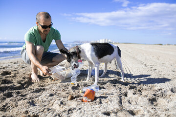Man and his dog cleaning the beach of plastic bottles