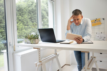 business man with blue shirt is standing behind high standing table and is working with his tablet