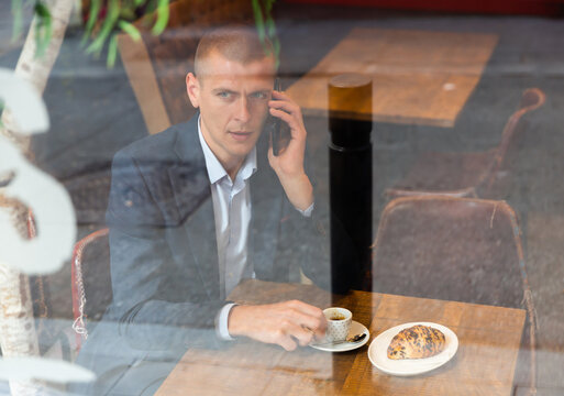 Portrait of elegant male businessman sitting in cafe with a cup of coffee and talking on phone