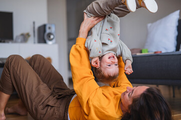 Young mother playing with small baby indoors at home, having fun.