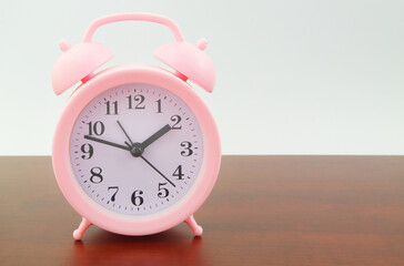 Pink alarm clock on wooden table, copy space for text.