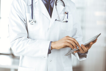 Unknown male doctor using tablet computer in clinic near his working place, closeup. Perfect medical service in hospital. Medicine and healthcare concept