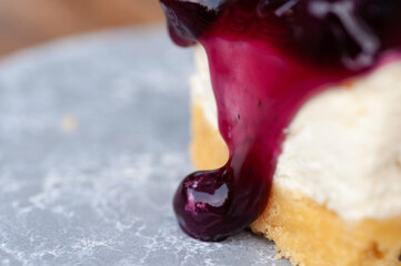Piece of cheesecake topping with black currant and blueberry sauce serve on white plate.