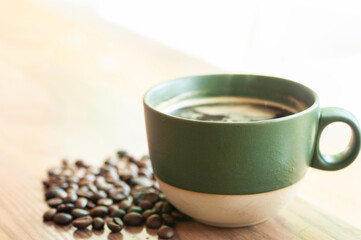 Hot coffee in two tone green and cream color ceramic cup with coffee bean on wooden table.