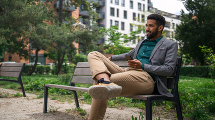 Obraz premium Portrait of cheerful young man with smartphone outdoors in city, resting.