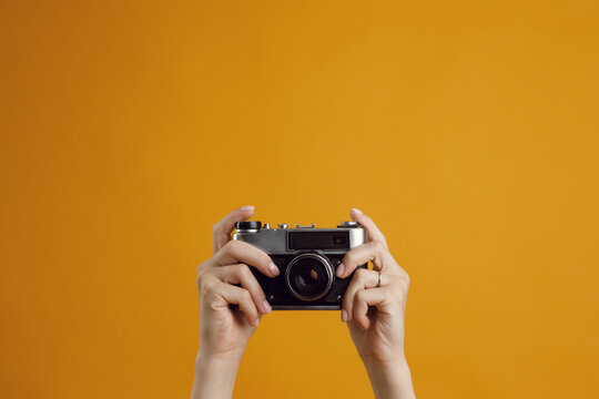 Classic 35mm old analog camera on yellow background. Hands of a girl with a camera, a place to copy.