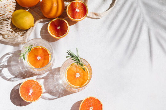 Summer orange cocktails with fresh citrus fruits. Hard seltzer, lemonade, refreshing drinks, low alcohol mocktails, summer party concept. Trendy shadow and sunlight. Flat lay, top view, copy space.